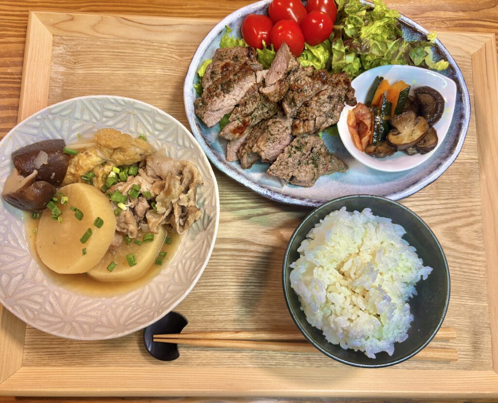 ラム肉ステーキと豚こま大根椎茸の煮物、ガーリック炒めサラダ、ご飯を並べた和洋ミックスの晩ごはんプレート
