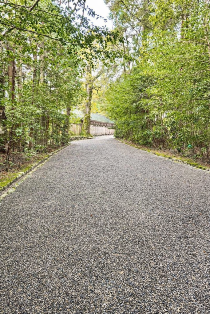 伊勢志摩の神社参道の風景。緑豊かな木々に囲まれた砂利道が続き、静寂で癒しを感じる散策スポット