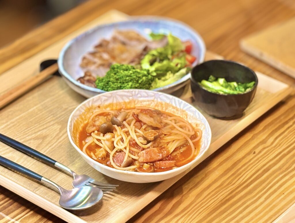 トマトジュースを使って時短かつ本格的に仕上げた、エビとベーコン、しめじ、新玉ねぎのトマトスープパスタ。奥には岩塩と小麦粉で美味しく焼いた絶品トンテキと、小松菜のガーリック炒めが並ぶ、ビールに合う晩酌の献立。