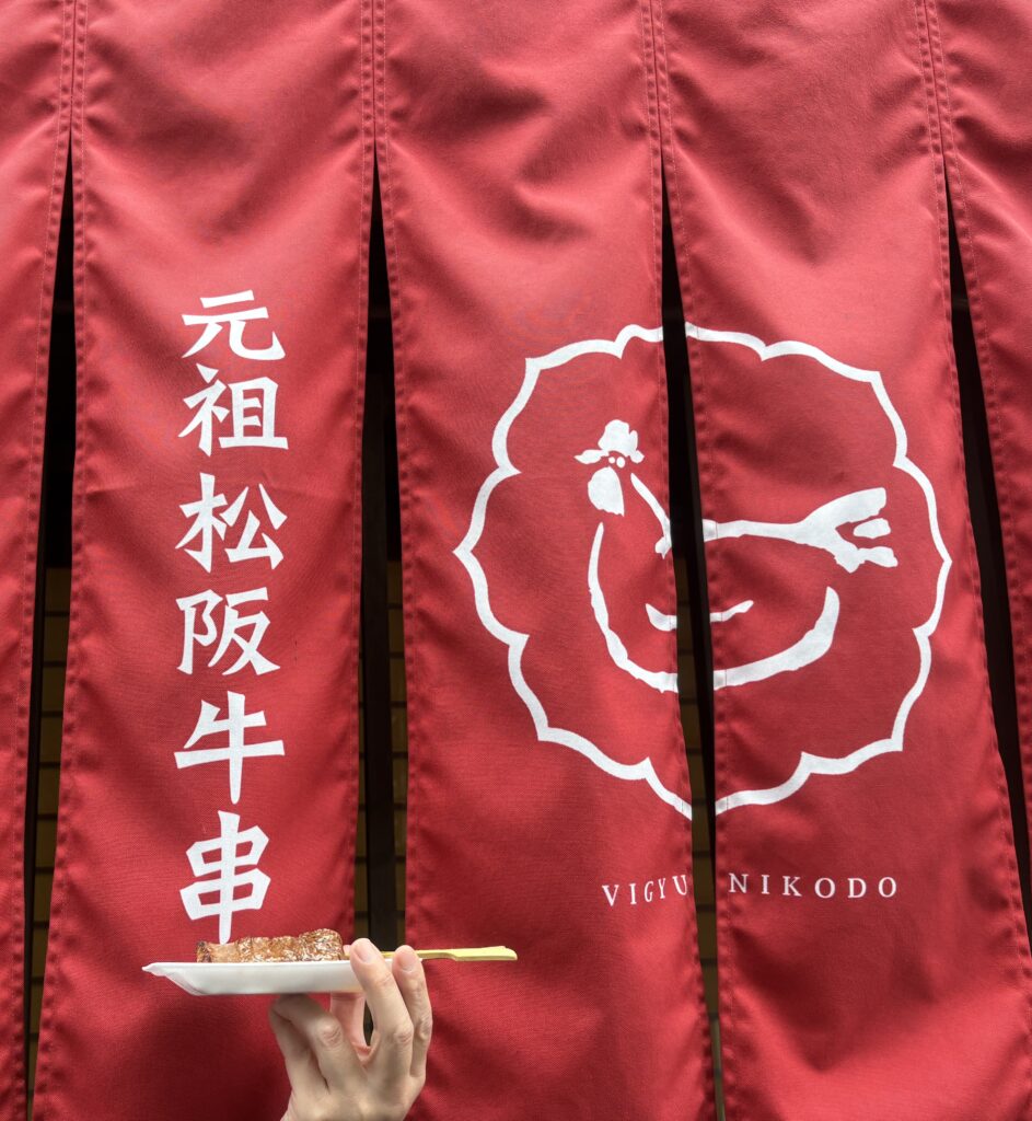おかげ横丁で食べ歩き!「元祖松阪牛串」と書かれた赤い大きなのれんの前に掲げた、焼き立てで美味しそうな松阪牛串