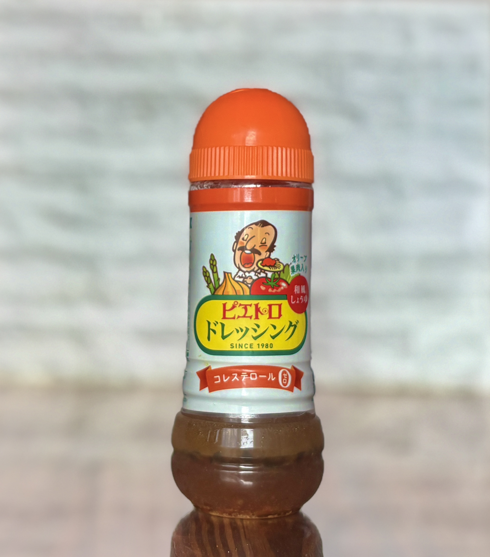 木製テーブルの上に置かれたピエトロドレッシング（和風しょうゆ味）のボトル。オレンジ色のキャップとイラスト入りラベルが特徴で、透明なボトル越しに具材入りのドレッシングが見える様子を正面から撮影。