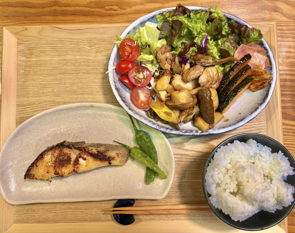 銀鱈の西京焼きを主菜にした和風の夕食献立。香ばしく焼き上げた銀鱈にししとうを添え、鳥もも肉と舞茸・エリンギのガリバタポン酢炒め、ベーコンとかぼちゃの炒め物、フレッシュサラダ、白ごはんを盛り付けたバランスの良い家庭料理。