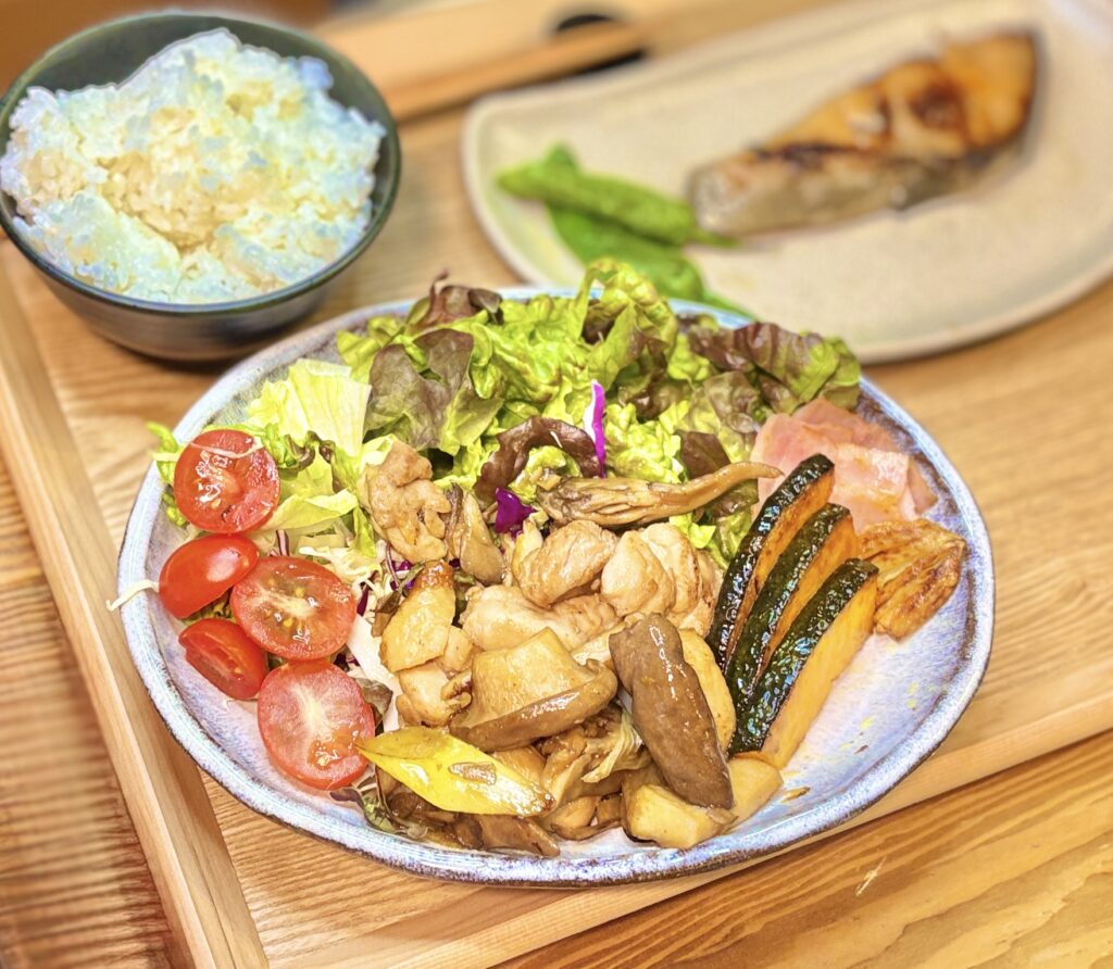 鳥もも肉と舞茸・エリンギをガーリックバターとポン酢で炒めた主菜風おかずに、ベーコンとかぼちゃの炒め物、レタスやミニトマトのサラダを添えた彩り豊かな一皿。食欲をそそるボリューム満点の家庭料理。
