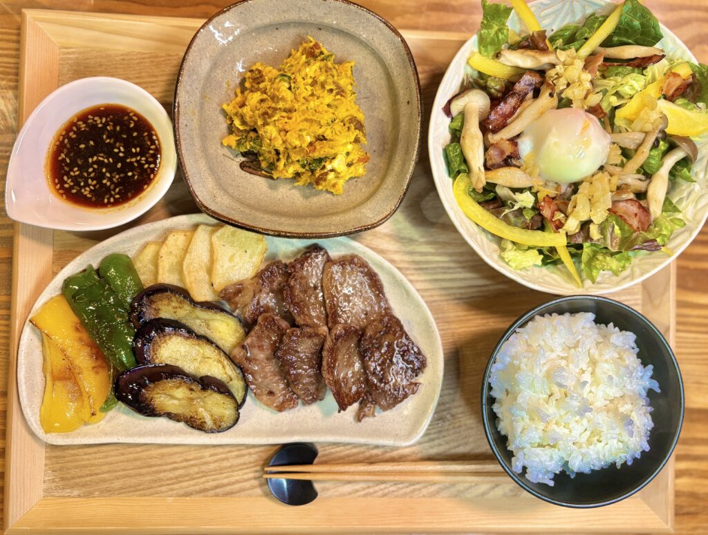 木のトレーの上に和牛ロースの焼肉と焼き野菜(茄子・パプリカ・スナップえんどう・長芋)のプレート、かぼちゃとクリームチーズのサラダ、ベーコンとしめじ