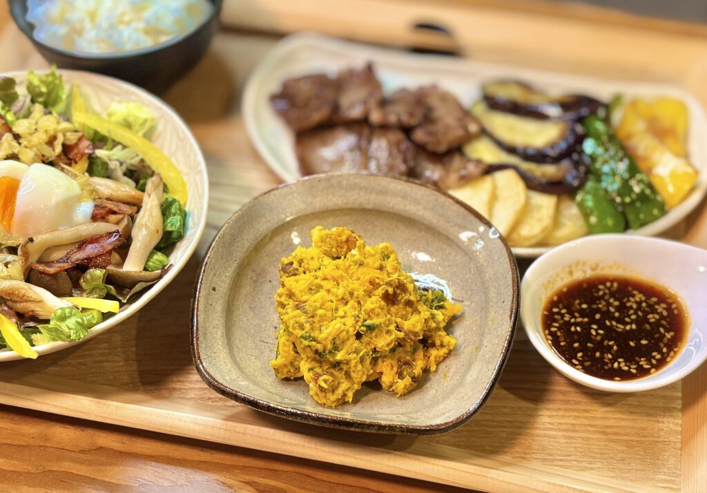 角皿に盛られたナッツとサルタナレーズン入りかぼちゃとクリームチーズのサラダ。奥に和牛焼肉と焼き野菜、温玉のせシーザーサラダ、ごまだれが並ぶ。