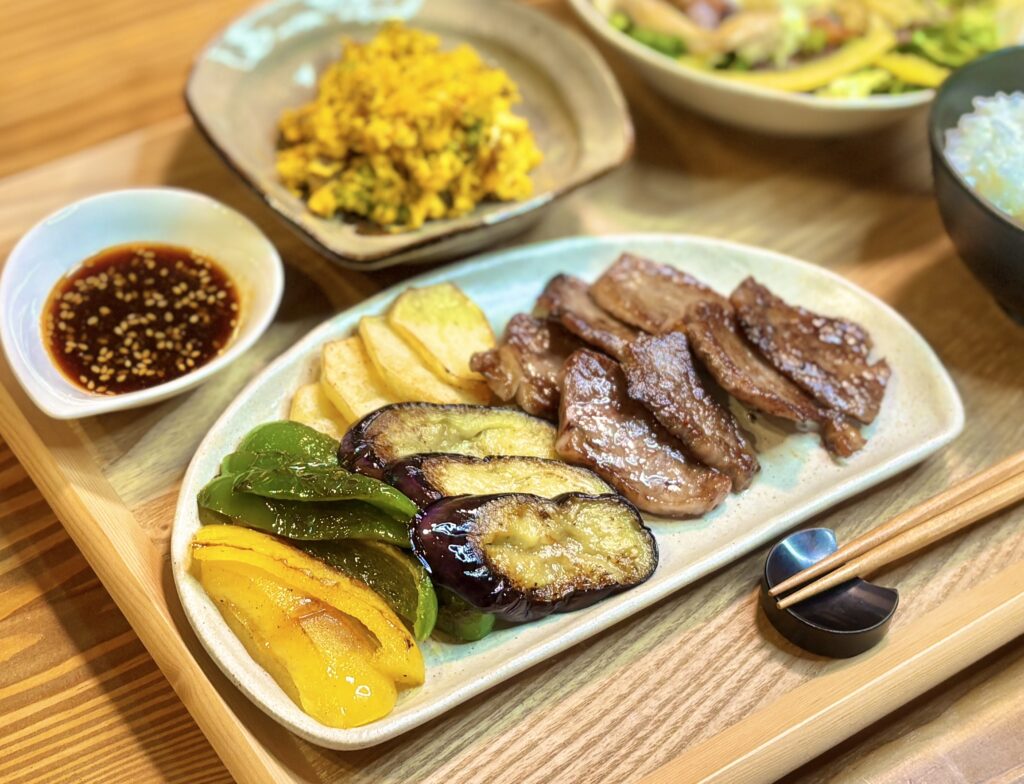 白いプレートに盛られた和牛ロースの焼肉と、茄子・パプリカ・スナップえんどう・長芋の焼き野菜。奥にかぼちゃサラダとシーザーサラダ、ごまだれが並ぶ旦那キッチンの献立。