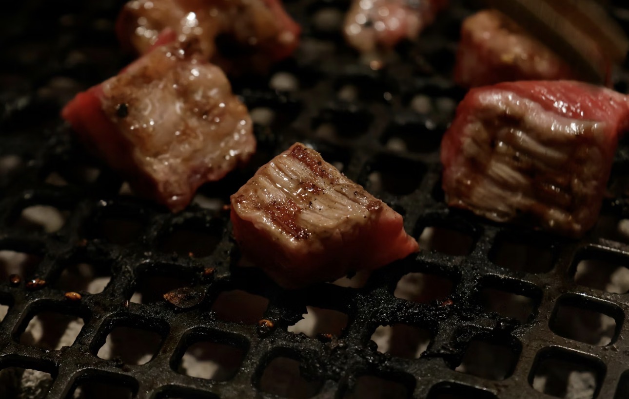 鉄板の上で焼かれている和牛ロースのサイコロステーキ。表面に焼き色がついてジューシーな断面が見えている。