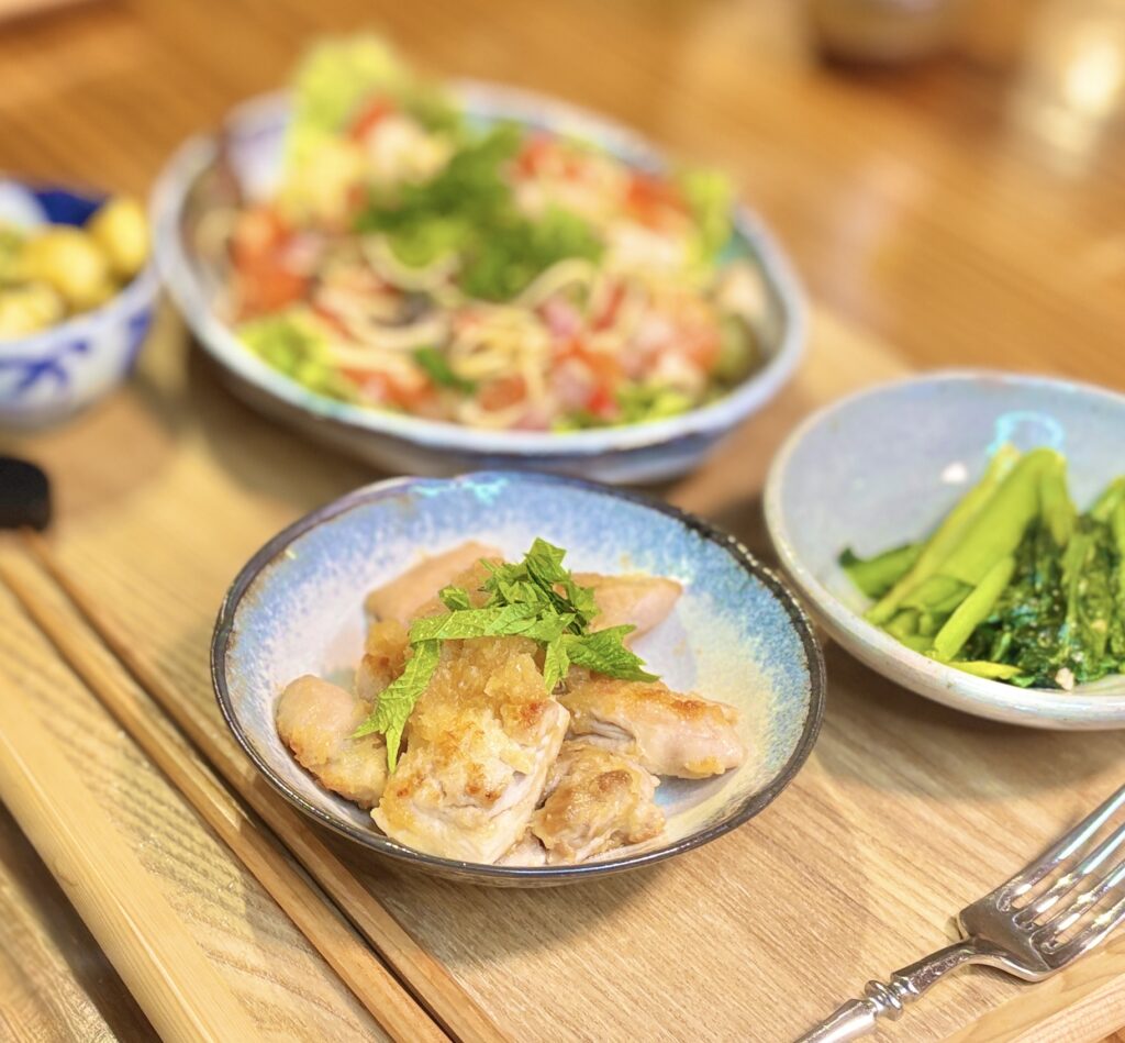 鶏もも肉の生姜みぞれ焼きに青紫蘇を乗せた一皿のアップ写真。大根おろしを汁ごと使った生姜焼きダレが絡んだやわらかジューシーな鶏もも肉に、爽やかな青紫蘇をトッピング。白ワインに合うさっぱりとした鶏料理レシピ。