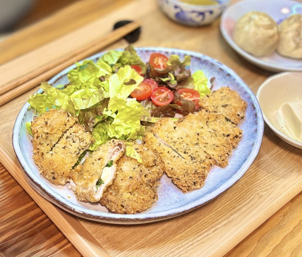 青紫蘇とチーズを挟んだ豚ロースのミラノ風カツレツ。サクサクの衣と野菜サラダが青みがかった大皿に盛り付けられている