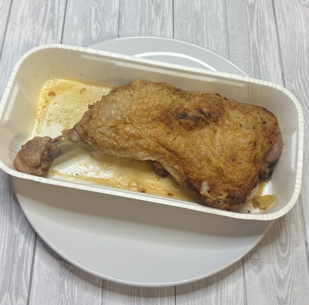 一鶴の骨付き鳥ひなを電子レンジで温めた直後の状態。紙製トレーに入ったまま白いお皿の上に置いており、黄金色に焼けた皮とにじみ出た旨みたっぷりのスパイスタレが確認できる。