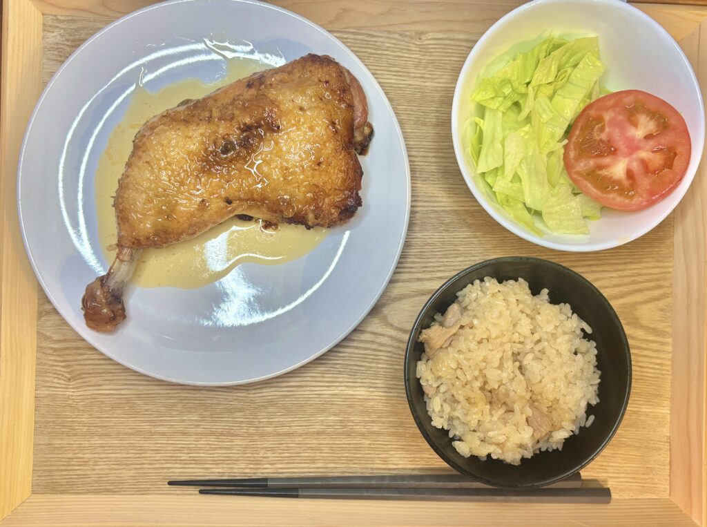 一鶴の骨付き鳥ひな、とり飯、野菜サラダを木のトレーに乗せた俯瞰ショット。お取り寄せとは思えない定食スタイルの豪華な盛り付け。