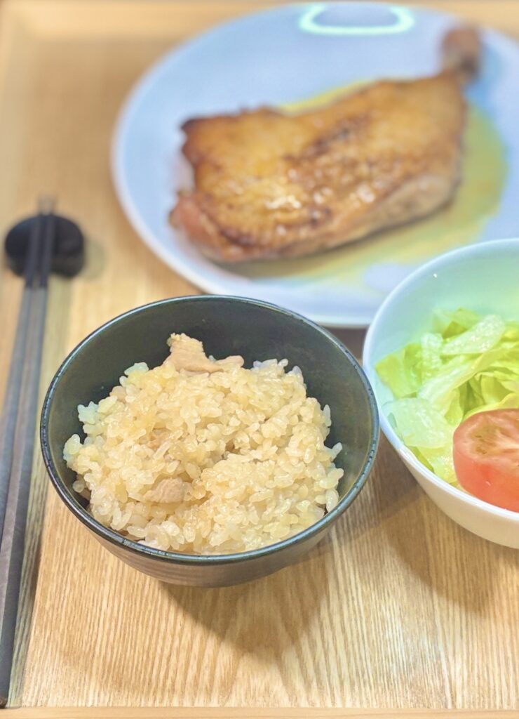 一鶴のとり飯を黒い茶碗によそった写真。手前にとり飯、奥に骨付き鳥ひなとサラダを配置。鶏の旨みがしっかり染み込んだとり飯の質感がよくわかる一枚。