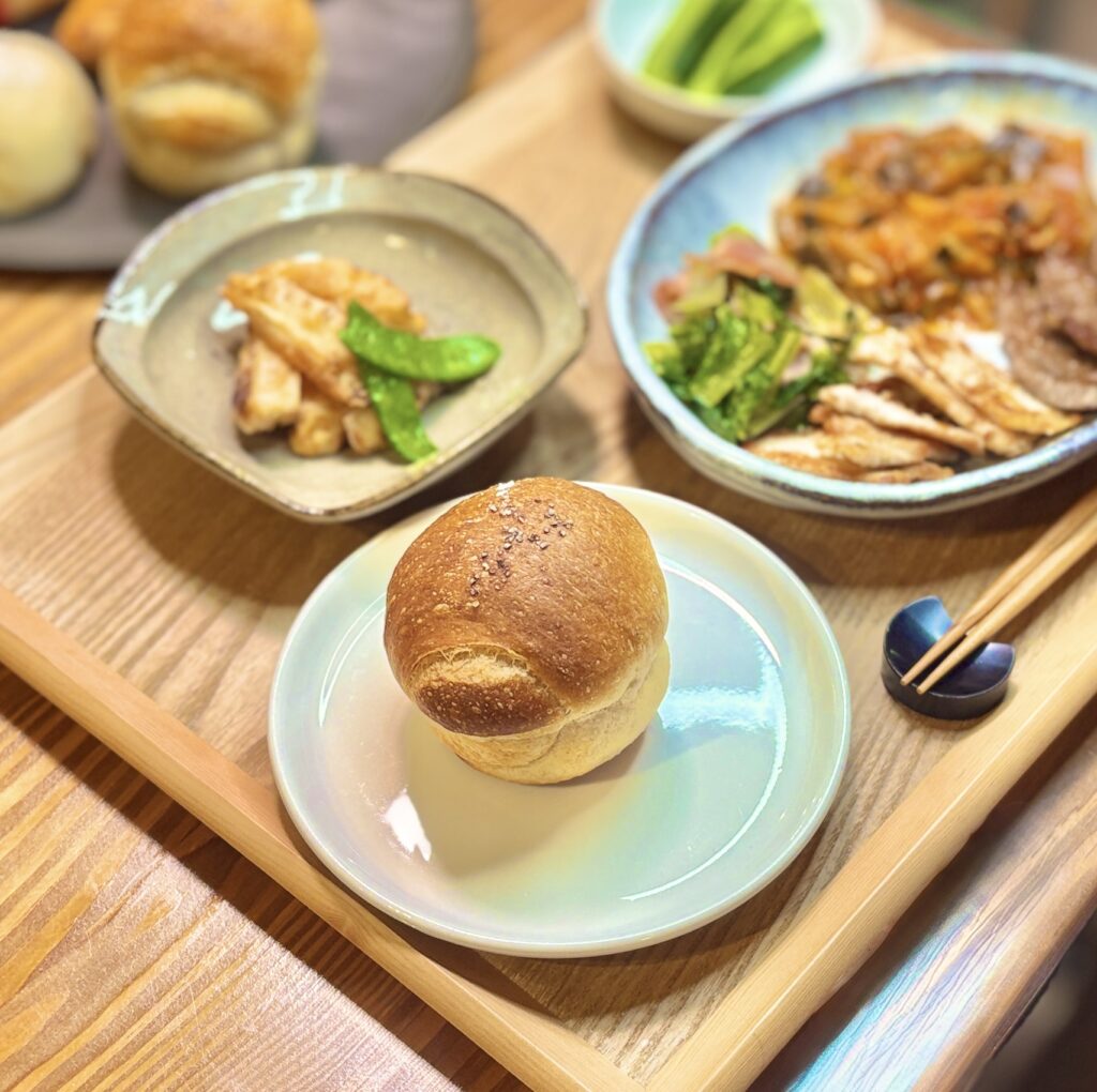 ブールアンジュ梅田のまるっとかわいい丸パンをアップで。奥にはタケノコの唐揚げとワンプレートが並ぶ