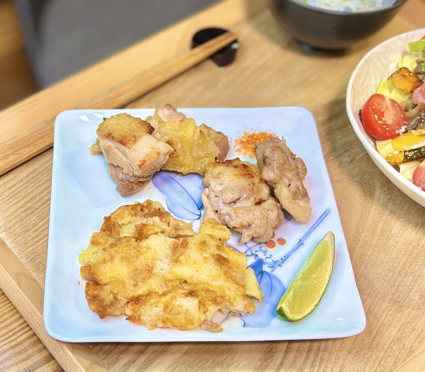 名古屋コーチンと国産若鶏を粉塩麹で焼いた食べ比べプレート。香ばしく焼き上げた塩麹チキンにライムを添え、同じ皿にはツナとチーズとポテトを混ぜてフライパンで焼いたポテト焼きも盛り付け。木製トレーの上に並んだ、白ワインに合う鶏肉料理と副菜の晩ごはん。