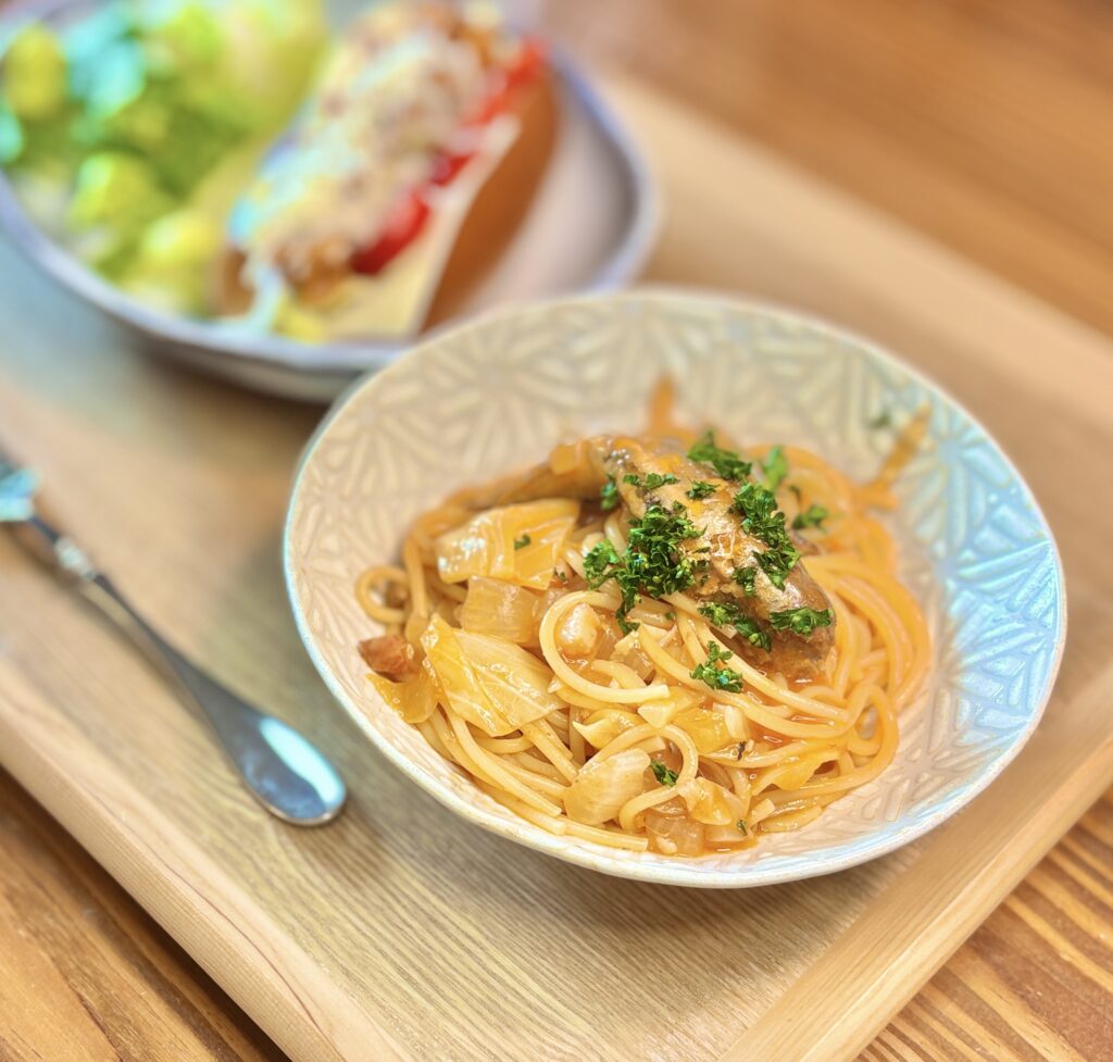 イワシのトマト缶を使ったガーリックトマトパスタと、チリビーンズチリドッグを一緒に楽しむ休日ランチ。トマトソースのパスタにイワシとパセリをのせ、チーズ入りチリドッグとロメインレタスを添えたおうちごはん。