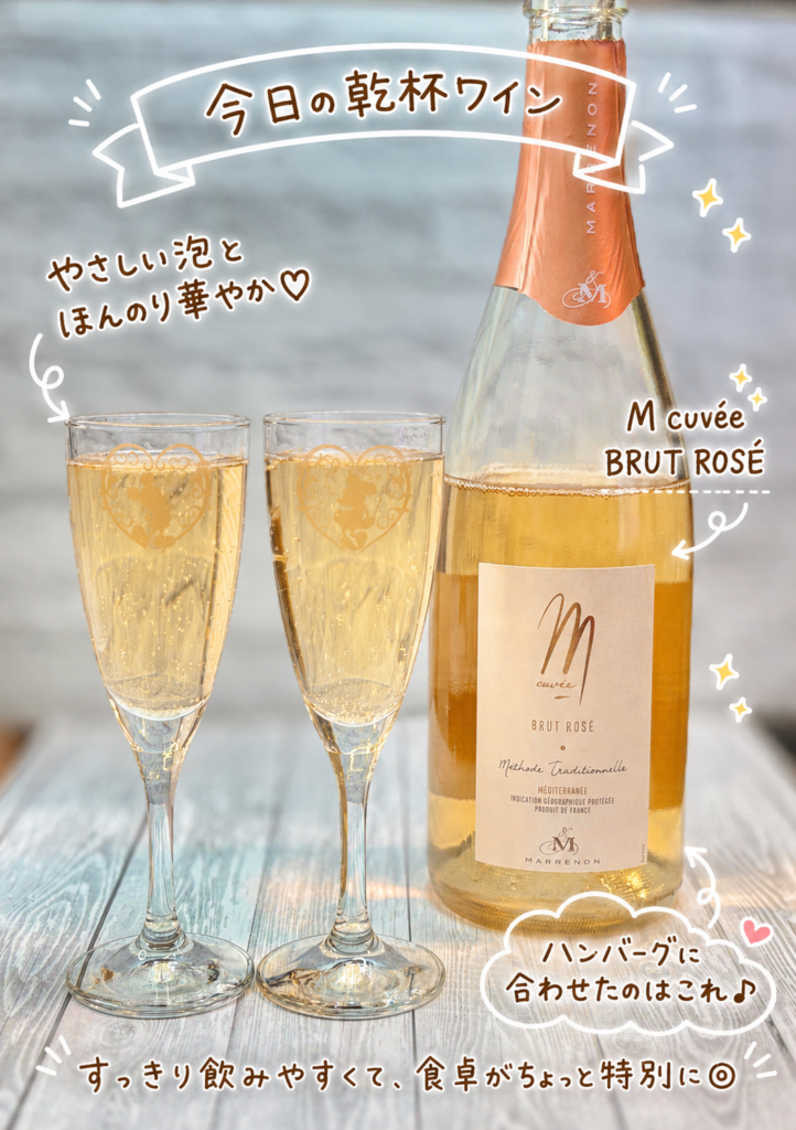 ハンバーグ献立に合わせたロゼスパークリングワイン、エム・キュヴェ ブリュット・ロゼ(M cuvée BRUT ROSÉ)と、グラスに注いだ乾杯ワインの写真。白いリボン風の文字入れで今日の乾杯ワインと紹介し、やさしい泡とほんのり華やかな味わい、ハンバーグに合わせたワインであることを可愛く表現しています。肉料理に合うワイン、ハンバーグに合うロゼスパークリング、辛口スパークリングワインのペアリングを紹介する記事にぴったりの画像です。