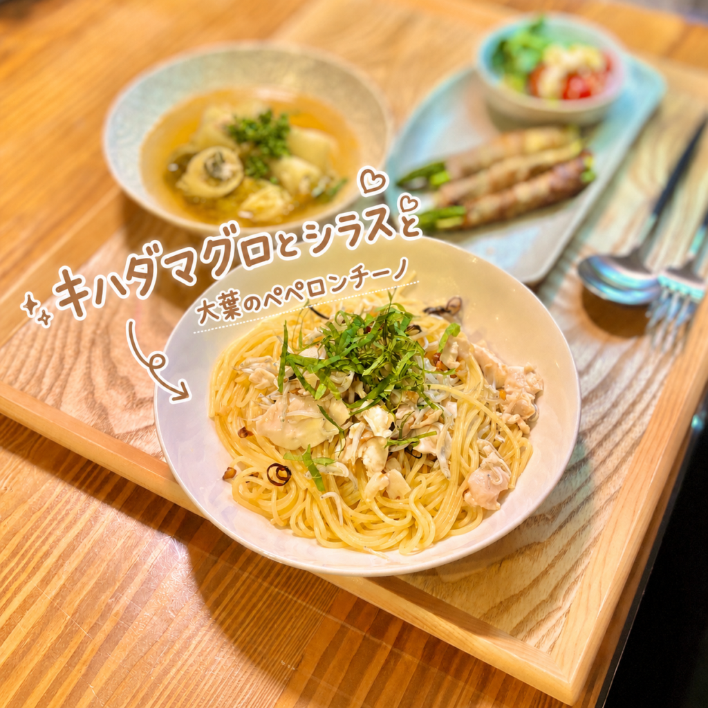 キハダマグロとシラスと大葉のペペロンチーノを中心にした、旦那キッチンの和風パスタ献立写真です。白い器には、細めのパスタにキハダマグロとシラスがたっぷり絡み、上には細切りの大葉がのせられています。魚介の旨み、シラスの塩気、大葉の爽やかな香りが合わさった、さっぱり食べられる和風ペペロンチーノです。背景には、豚バラ肉と白菜のロール出汁煮やアスパラ豚バラ巻き、カプレーゼ風の副菜が並び、主食とおかずがバランスよくそろった晩ごはんの雰囲気が伝わります。写真には、キハダマグロとシラスと大葉のペペロンチーノという可愛い文字入れと矢印、ハートの装飾があり、料理ブログのメイン画像にも使いやすい一枚です。キハダマグロパスタ、しらす大葉ペペロンチーノ、和風ペペロンチーノ、魚介パスタ、家庭料理の献立、旦那キッチン晩ごはんとして紹介する画像に適しています。