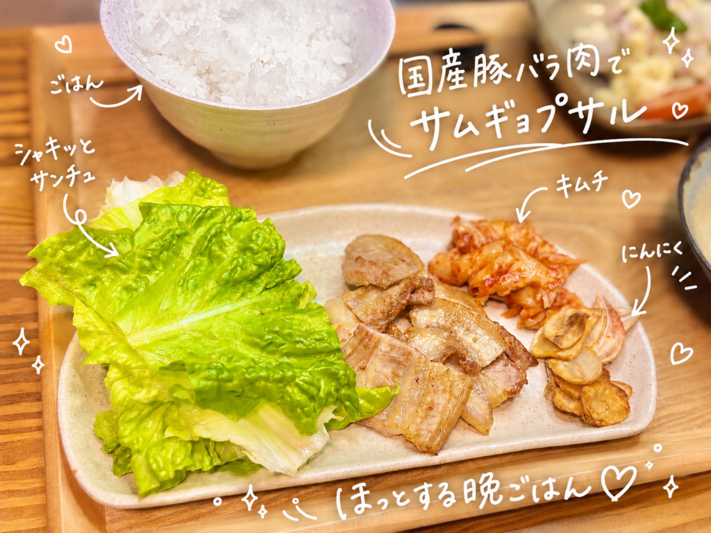国産豚バラ肉のサムギョプサルを、サンチュ、キムチ、焼きにんにく、白ごはんと一緒に盛り付けた晩ごはんのアップ写真。香ばしく焼いた豚バラ肉をサンチュで巻いて楽しめるおうちサムギョプサル献立で、キムチの辛みとにんにくの香ばしさが豚バラ肉の旨みを引き立てる、ビールにも合う家庭料理として紹介した手書き風文字入り画像。