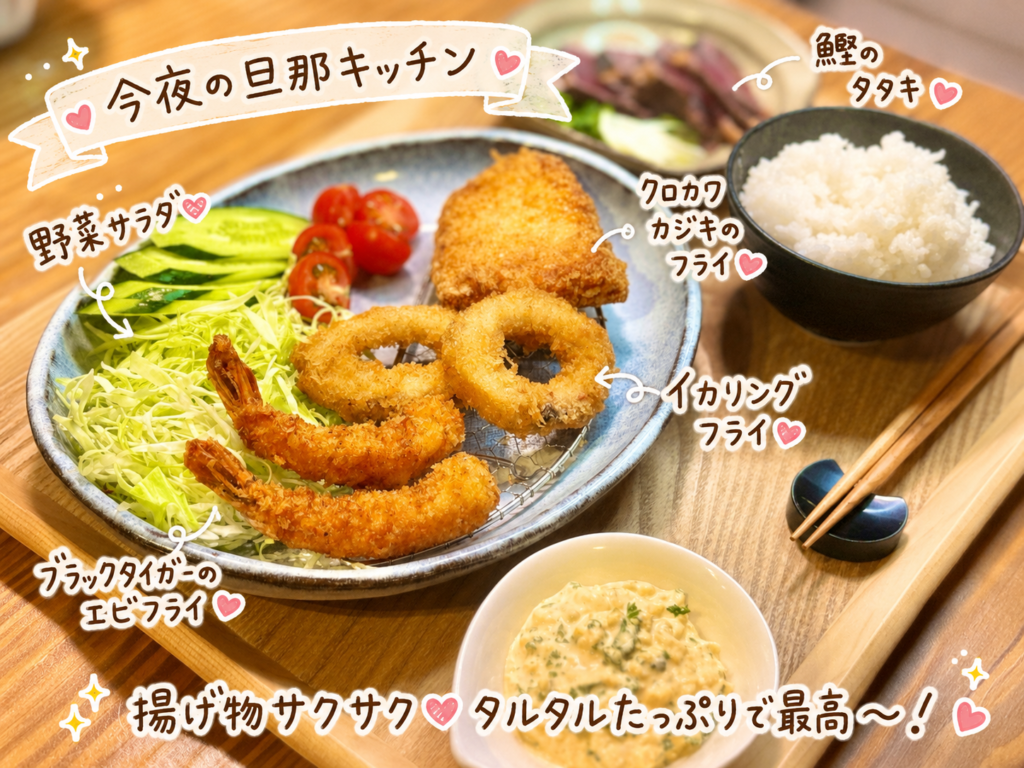旦那キッチンのフライ三種盛り献立を別アングルから撮影。網付きの大皿にブラックタイガーのエビフライ・イカリングフライ・クロカワカジキのフライがきつね色に揚がり、キャベツ千切り・きゅうり・ミニトマトの野菜サラダと一緒に盛り付けられている。右奥にかいわれ大根を添えた鰹のタタキ、手前にたっぷりの手作りタルタルソース、奥に白ごはんが並ぶ、ビールにも白ワインにも合う揚げ物献立。
