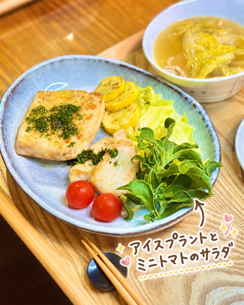 アイスプラントとミニトマトのサラダを可愛く紹介した、旦那キッチン晩ごはんの副菜写真です。淡いブルーの器には、クロカワカジキとメバチマグロのムニエル、黄色ズッキーニのソテー、レタス、アイスプラント、ミニトマトが彩りよく盛りつけられています。写真右下には、アイスプラントとミニトマトのサラダという手書き風の文字入れと矢印、ハートやきらきらの装飾があり、爽やかな副菜の雰囲気が伝わります。アイスプラントのシャキッとした食感と、ミニトマトのみずみずしい赤色が、魚のムニエルやレモンパセリバターソースのコクを軽やかに引き立ててくれそうな一皿です。アイスプラントレシピ、ミニトマトサラダ、魚料理に合う副菜、ムニエル献立、彩り野菜のサラダ、旦那キッチンの家庭料理ブログに適した画像です。