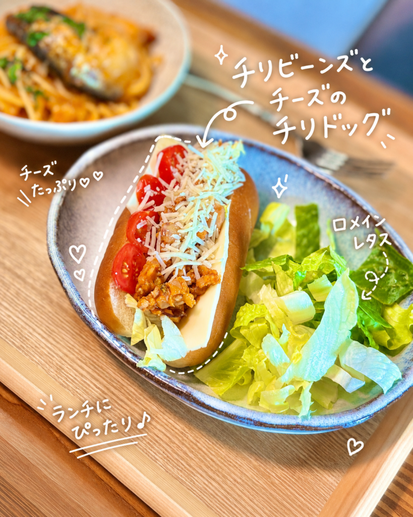 チリビーンズとチーズを挟んだチリドッグに、ミニトマトと細切りチーズをのせ、ロメインレタスを添えた休日ランチ。タコス用のひき肉と豆のトマトチリ煮込みをアレンジした、食べごたえのあるホットドッグ。