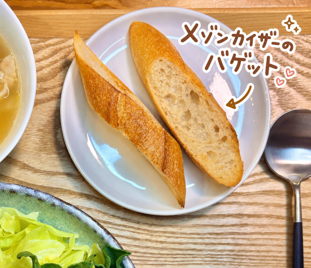 メゾンカイザーのバゲットを白いお皿に盛りつけた、旦那キッチン晩ごはんの一品写真です。木製トレーの上に、香ばしい焼き色のついたバゲットが2切れ並んでおり、外側のパリッとしたクラストと、中の気泡が見えるふんわりした生地感が伝わります。写真右上には、メゾンカイザーのバゲットという可愛い手書き風の文字入れと矢印、ハートやきらきらの装飾が入っていて、パンの美味しさを楽しく紹介する雰囲気になっています。クロカワカジキとメバチマグロのムニエル、レモンパセリバターソース、白菜と豚バラのスープに添えるパンとして、洋食献立やおうちビストロ風の食卓にぴったりです。バゲットに合う料理、メゾンカイザーのパン、魚料理に合わせるパン、ムニエル献立、旦那キッチンの晩ごはん記事に適した画像です。