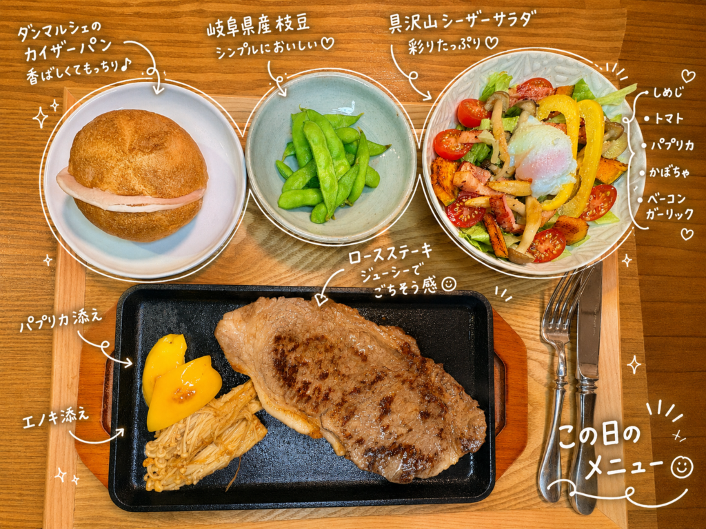 ロースステーキをメインに、パプリカとエノキを添えた鉄板ステーキ、温泉卵のせ具沢山シーザーサラダ、岐阜県産枝豆、ダンマルシェのカイザーパンを木製トレーに並べたおうちごちそうディナーの献立写真。黒い鉄板プレートにのったジューシーなロースステーキを中心に、彩り豊かなサラダや枝豆、香ばしいカイザーパンを組み合わせた、赤ワインにも合う旦那キッチンのおうちごはんメニュー。