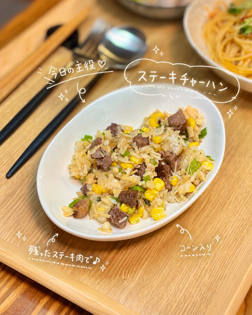 残ったステーキ肉で作る贅沢なステーキチャーハン。コーンと刻みネギが散りばめられた黄金色のチャーハンが白い楕円皿に盛り付けられ、木製のトレーの上に置かれている。旦那キッチン流・牛肉リメイクレシピ。