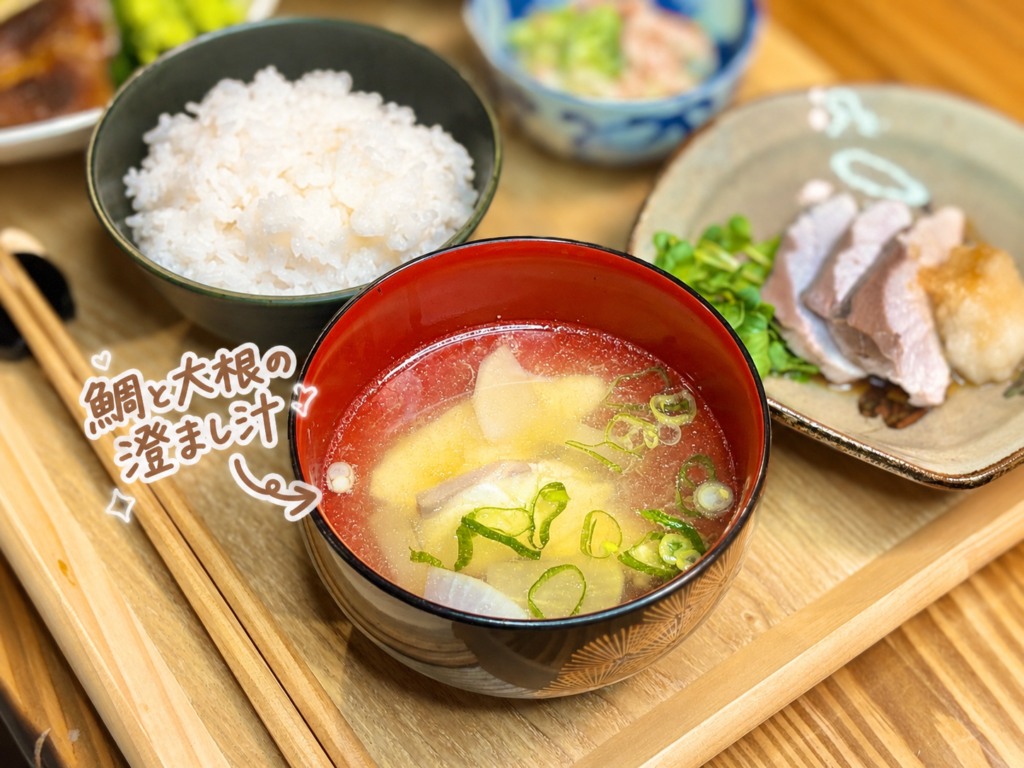 鯛と大根の澄まし汁を主役にした、温かみのある和食の汁物写真です。赤いお椀には、透明感のある出汁に鯛、大根、青ねぎが入っており、鯛の上品な旨みと大根のやさしい甘みが感じられる一杯です。写真には、鯛と大根の澄まし汁という可愛い手書き風の文字入れと矢印、ハートやきらきらの装飾が入っていて、汁物の内容がひと目でわかります。背景には白ごはんやぶりのおろししゃぶしゃぶ、カニカマきゅうりが見え、3種のしゃぶしゃぶ御膳をやさしくまとめる汁物として自然に紹介できます。鯛の澄まし汁、大根の澄まし汁、和食の汁物、しゃぶしゃぶ献立、旦那キッチンの家庭料理ブログに適した代替テキストです。