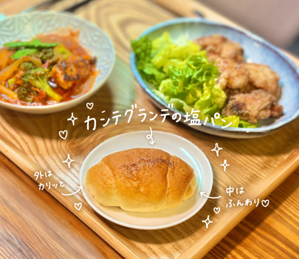 カンテグランデの塩パンをメインに写した旦那キッチンの晩ごはん写真。外はカリッと香ばしく、中はふんわりした塩パンを白い皿に盛り付け、奥には有吉ゼミ高砂部屋風の白だし唐揚げと、鶏肉とブロッコリーのトマト煮を添えたカフェ風の食卓。塩パンをトマト煮のソースに合わせて楽しむ、おうちごはんとパンの相性を紹介する写真。