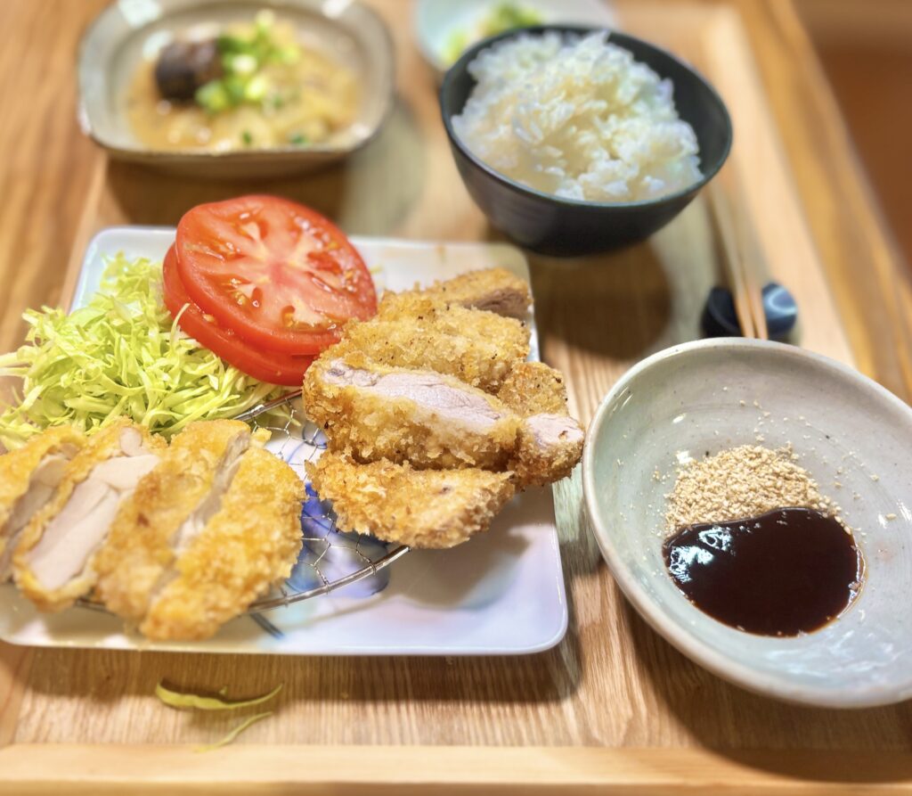 サクサクに揚げた豚ヒレカツとチキンカツに、千切りキャベツ、トマトスライス、ソースとすりごまを添えたおうち揚げ物定食