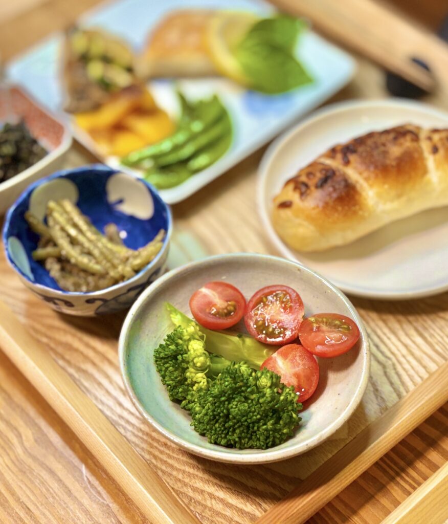 ブロッコリーとミニトマトの副菜を中心に、真鯛のムニエル レモンバターソース、焼き野菜、ふきのナムル、コープの塩バターチーズパンを合わせた旦那キッチンのおうちビストロ風晩ごはん。