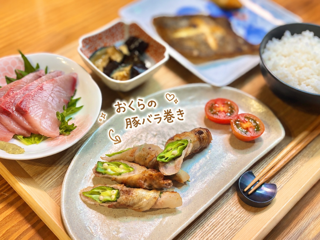 おくらの豚バラ巻きとミニトマトを淡い色のお皿に盛り付けた写真。手書き風の文字で料理名を紹介し、断面から見えるおくらの緑がきれいな、肉巻きおかずと和食献立の一品画像。