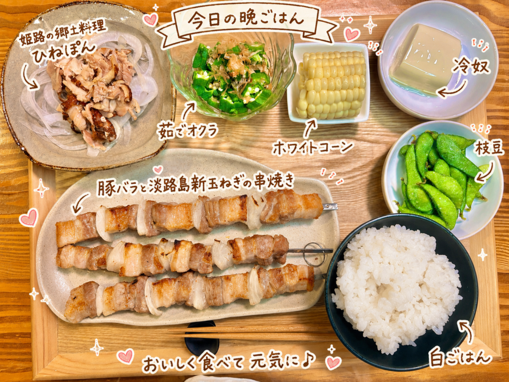 豚バラと淡路島新玉ねぎの串焼き、姫路の郷土料理ひねぽん、茹でオクラ、ホワイトコーン、冷奴、枝豆、白ごはんを木のトレーに並べた旦那キッチンの晩ごはん献立写真。手書き風の文字で料理名を可愛く紹介している。