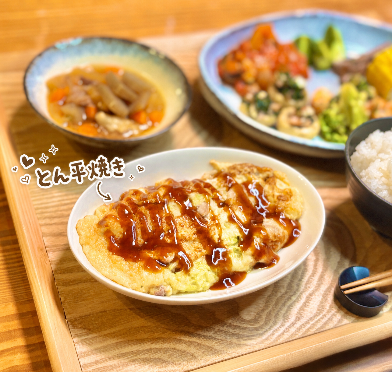 とん平焼き、牛スジ煮込み、マッシュルームのセゴビア風、エビとブロッコリーのガーリックチーズ炒め、ラタトゥユ、牛肉の紫蘇巻き、とうもろこし、白ごはんを並べた、品数たっぷりの旦那キッチン晩ごはん献立。