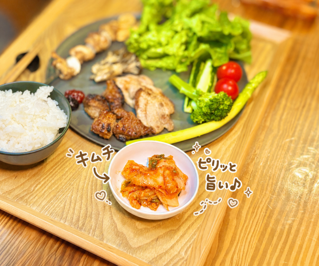 キムチを小皿に盛りつけ、奥に焼肉プレートと白ごはんを添えた食卓を、手書き風の可愛い文字で紹介した写真