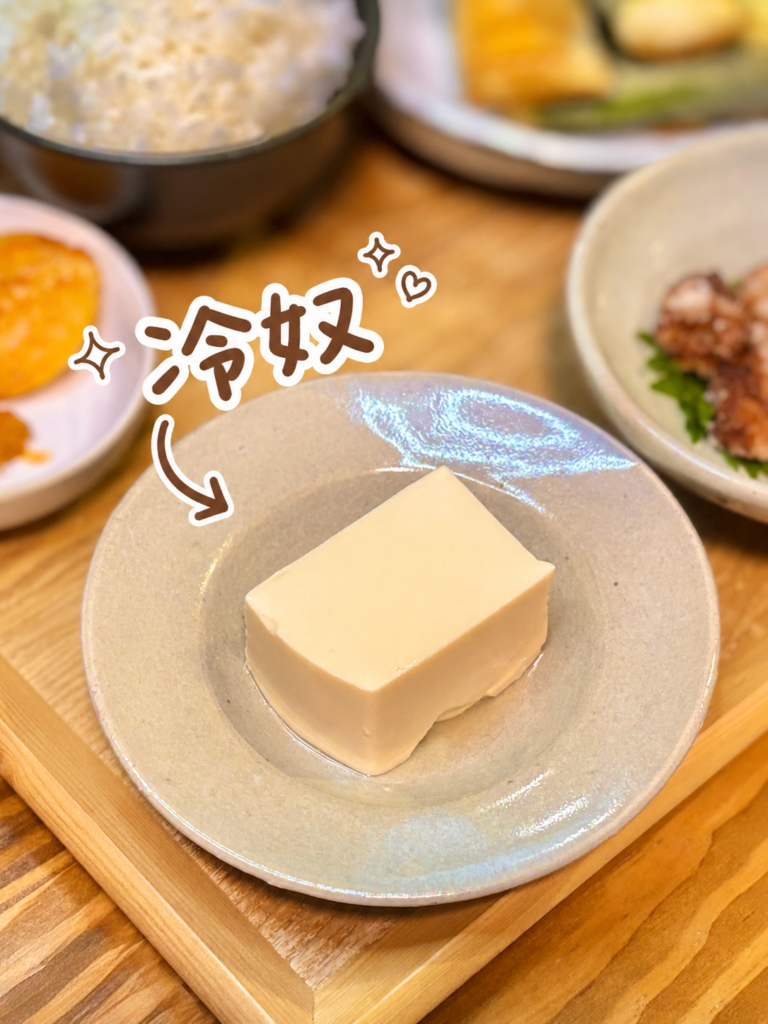 なめらかな豆腐を小皿に盛り付けた冷奴の写真。手書き風の文字と矢印で冷奴を可愛く紹介し、唐揚げや春巻きなど揚げものが多い献立の中で、さっぱり食べられる箸休めとして見せた一品画像。