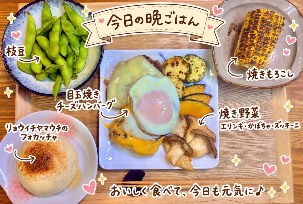 目玉焼きチーズハンバーグ、焼き野菜、焼きもろこし、枝豆、リョウイチヤマウチのフォカッチャを木のトレーに並べた洋食プレート献立の写真。手書き風の文字でメニュー名を可愛く紹介している