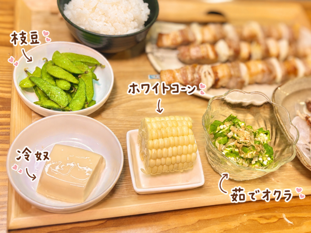 枝豆、冷奴、ホワイトコーン、茹でオクラを木のトレーに並べた副菜写真。豚バラ串焼きやひねぽんに合わせた、さっぱり食べやすい副菜を手書き風の文字で可愛く紹介している。