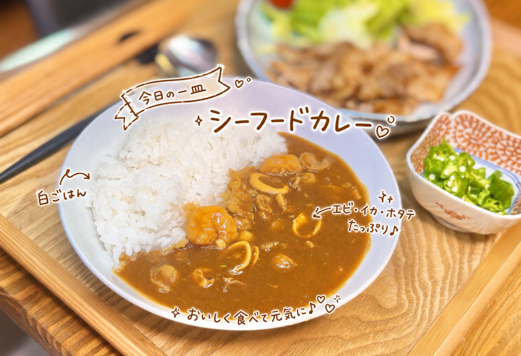 白ごはんにエビ・イカ・ホタテ入りのシーフードカレーをかけた一皿。魚介の旨みたっぷりのカレーに、手書き風の文字でメニュー名を添えた晩ごはん写真