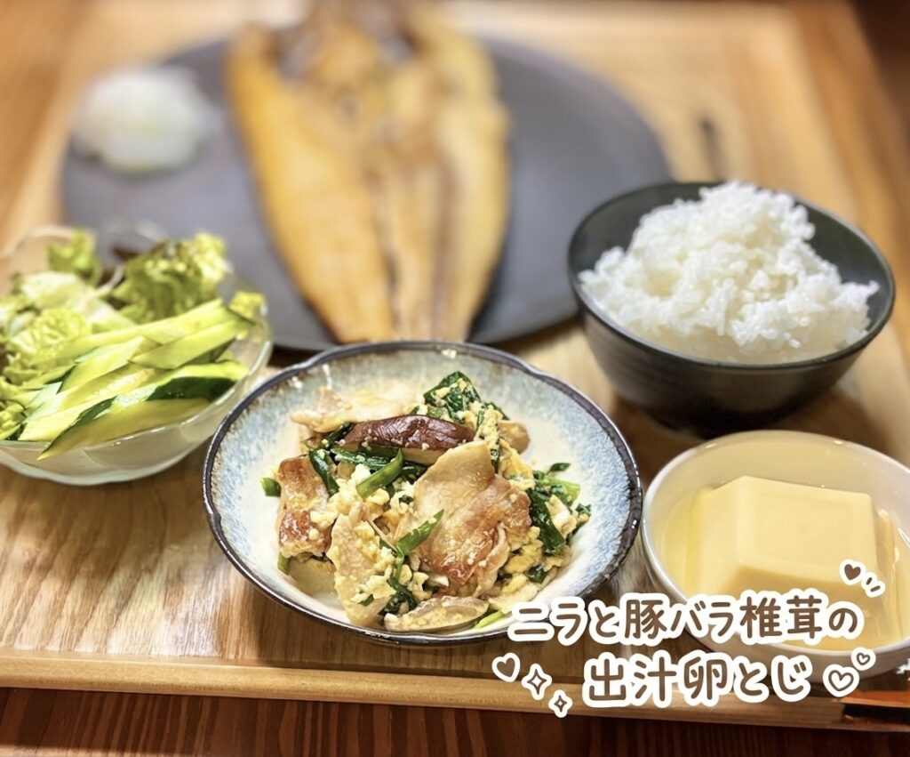 ニラと豚バラ椎茸の出汁卵とじを中心にした、和食副菜の写真です。器には、豚バラ肉、ニラ、椎茸、卵が出汁でふんわりとじられており、豚バラの旨み、椎茸の香り、ニラの風味が白ごはんに合いそうな一品として伝わります。背景には、ほっけの塩焼き、野菜サラダ、白ごはん、卵豆腐が並び、焼き魚メインの和食献立に満足感を添える副菜として紹介できます。写真には「ニラと豚バラ椎茸の出汁卵とじ」という可愛い手書き風の文字入れと、ハートやきらきらの装飾が入っており、料理ブログらしい温かい雰囲気があります。ニラ卵とじ、豚バラ卵とじ、椎茸レシピ、出汁卵とじ、ほっけの塩焼き献立、おうちごはん、旦那キッチンの記事に適した画像です。
