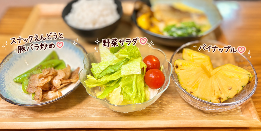 真鯛のガーリッククリームソースに合う副菜として、スナックえんどうと豚バラ炒め、野菜サラダ、パイナップルを並べた献立