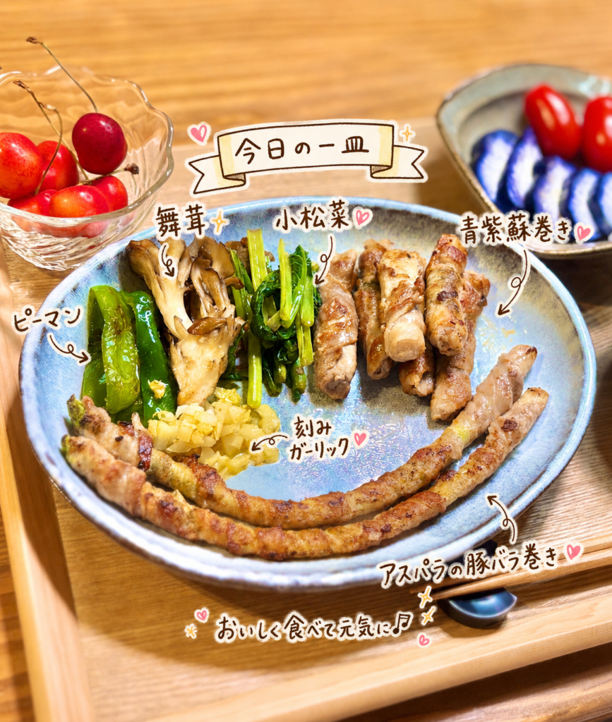 アスパラの豚バラ巻きと薄切り豚ロース肉の青紫蘇巻きをアップで写した写真。小松菜、ピーマン、舞茸、刻みガーリックを添えた香ばしい豚肉巻きの一皿を、手書き風の文字で紹介している。