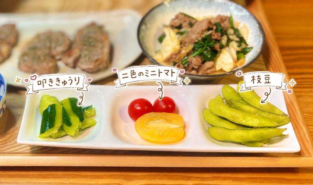 叩ききゅうり、赤と黄色の二色のミニトマト、枝豆を三つ仕切りの白い器に盛りつけた写真。ラム肉献立に添えた彩りのよい副菜を、手書き風の文字で可愛く紹介している