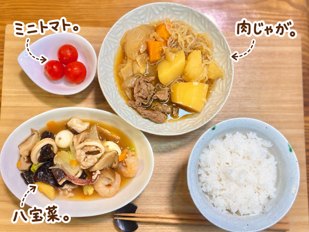 牛肉とじゃがいも、玉ねぎ、にんじん、しらたきの肉じゃがと、えび・いか・豚肉・うずら卵・きのこ・野菜たっぷりの八宝菜、ミニトマト、白ごはんを並べた家庭料理の晩ごはん献立