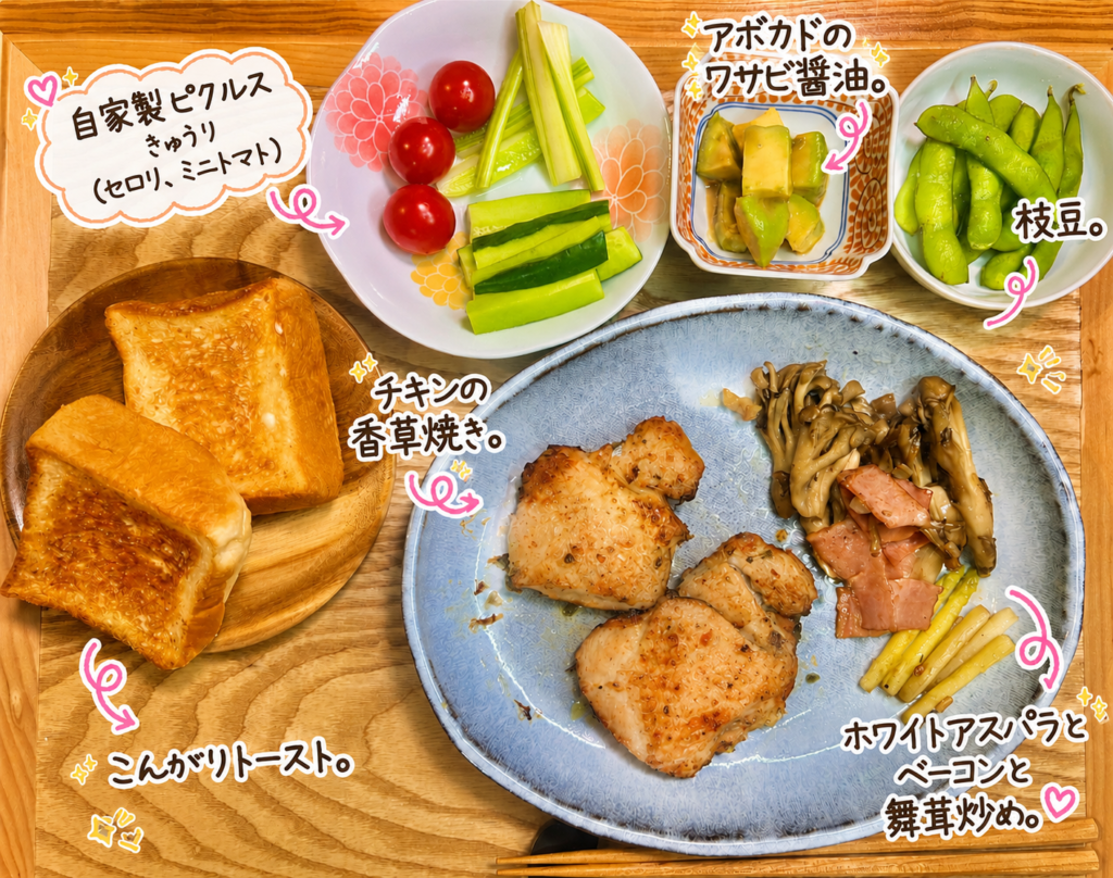 チキンの香草焼きをメインに、ホワイトアスパラとベーコンと舞茸炒め、自家製ピクルス、アボカドのわさび醤油、枝豆、こんがりトーストを添えた彩り豊かな献立。おうちカフェ風のワンプレート夕食。