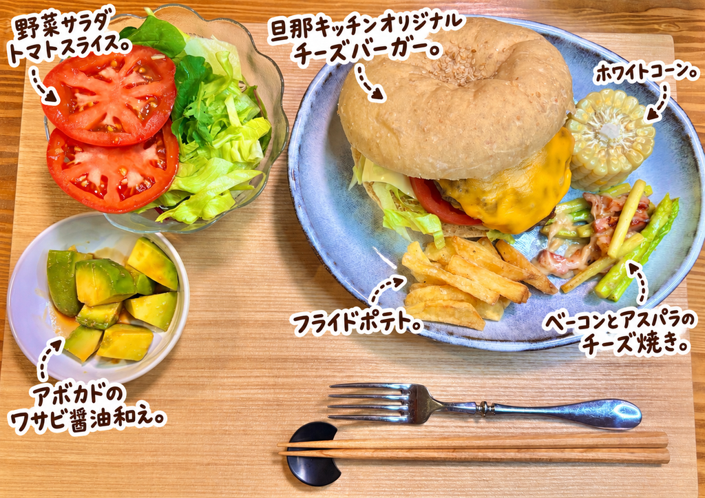 旦那キッチンオリジナルの手作りチーズバーガーを主役に、フライドポテト、ホワイトコーン、ベーコンとアスパラのチーズ焼き、アボカドのわさび醤油和え、トマトスライス入り野菜サラダを並べたボリューム満点の晩ごはん献立