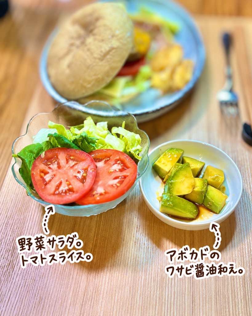 トマトスライスとレタスを盛り付けた野菜サラダと、角切りアボカドをわさび醤油で和えた簡単副菜。手作りチーズバーガーに合わせた、さっぱり食べられる野菜とアボカドの付け合わせ